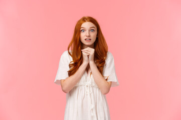 Hopeful and amused, redhead female in white dress, holding hands together over chest in praying...