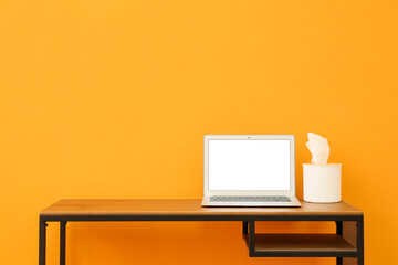 Modern workplace with laptop and tissue box near color wall