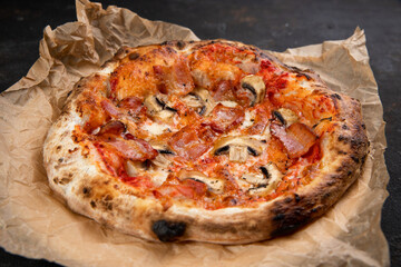Delicious pizza with bacon and mushrooms mushrooms fresh Pastries on a black concrete background. Top view of a hot pepperoni pizza. With space for text. He was lying flat. Ruddy dough on kraft paper 