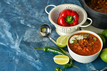 Bowl with delicious chili con carne and lime on grunge background