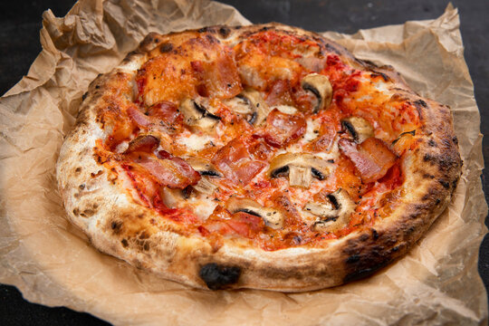 Delicious pizza with bacon and mushrooms mushrooms fresh Pastries on a black concrete background. Top view of a hot pepperoni pizza. With space for text. He was lying flat. Ruddy dough on kraft paper 