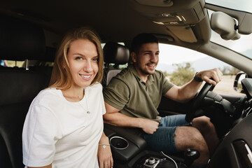 Beautiful young couple sitting on front passenger seats and driving a car