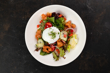 A beautiful fresh salad with salmon red fish vegetables lettuce leaves poached egg cucumbers bell peppers olives red onions is decorated on a white plate on a black background close up