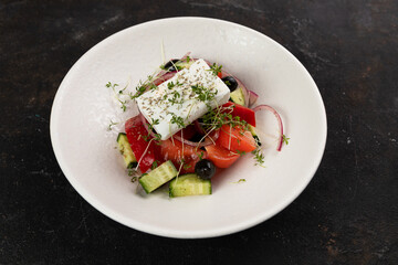 Greek salad with Feta cheese, red onion, tomatoes , cucumbers , olive oil, close-up, olives, in a white plate on a black background frame from above 