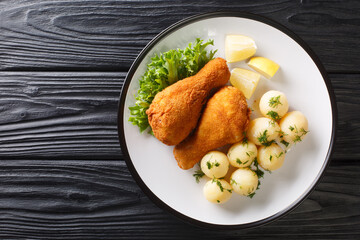 Austrian Fried Chicken Backhendl served with lemon and new potatoes close up in the plate on the table. Horizontal top view from above