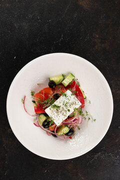 Greek salad with Feta cheese, red onion, tomatoes , cucumbers , olive oil, close-up, olives, in a white plate on a black background frame from above 