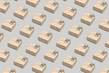 Pattern made of small gift boxes wrapped in craft paper with dried eucalyptus leaves on solid gray background. Modern minimal presents suitable for any occasion Neutral holiday backdrop Isometric view