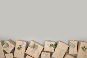 Small gift boxes wrapped in craft paper with dried eucalyptus leaves on solid gray background. Modern minimal presents suitable for any occasion. Neutral holiday backdrop with copy space.