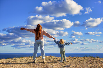 Mother and daughter holding hands and looking up admiring the amazing clouds over the sea. Travel...