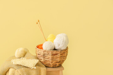 Basket with knitting yarn, needles and plaid on step ladder against color background
