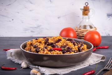 Mexican tomato rice with beans in a plate on the table with tomatoes and hot peppers on the table.