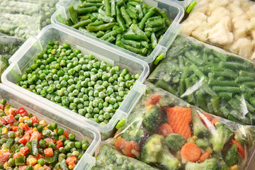 Plastic bags and containers with different frozen vegetables as background