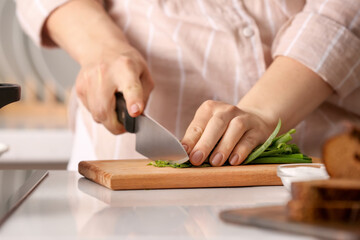 Woman cutting greens on wooden board in kitchen