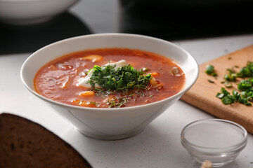 Bowl with delicious borscht, sour cream and greens on table in kitchen