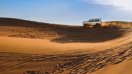 White jeep driving through the desert sand dunes on the background of the sky - obrazy, fototapety, plakaty