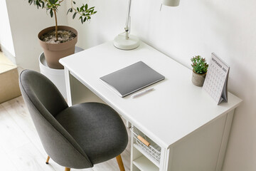 Modern workplace with lamp, notebook and calendar near white wall