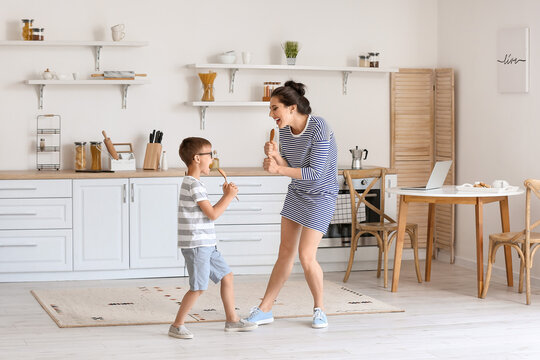 Young woman and her little son dancing and singing in kitchen