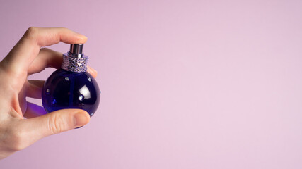 Small blue perfume bottle on violet. Cologne jar on purple. Mini bottle of perfume in hand with...