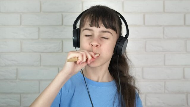 A teenager brushes his teeth and listens to music. A cute teenage girl in headphones and brushes her teeth with a wooden brush.
