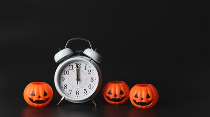 white vintage alarm clock show 12 o'clock  with halloween pumpkins on black background. Halloween...