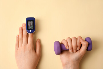 Female hands with pulse oximeter and dumbbell on color background