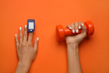 Female hands with pulse oximeter and dumbbell on color background