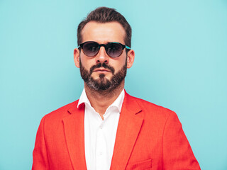 Closeup portrait of handsome confident stylish hipster lambersexual model.Sexy modern man dressed in elegant red suit. Fashion male posing in studio near blue wall in sunglasses