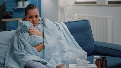 Unhappy woman shivering because of cold and flu, using blanket and pillow for warmth. Sick adult...