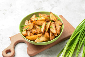 Bowl of tasty baked potato with green onion on light background