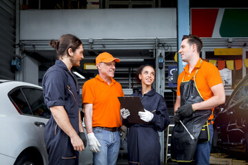 Group of four car service technician men and woman talking at workplace, people working together at vehicle repair garage service shop, check and repair customer car at automobile service center