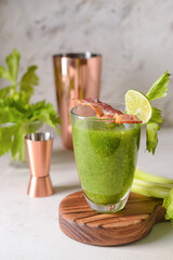 Glass of bloody Mary cocktail garnished with bacon on light background