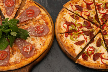 Two pizza composition. Delicious mixed ingredients Italian pizza, red and green pepper slices and sucuk, pepperoni. And pizza with smoked meat and tomatoes, with arugula leaves.