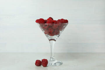 Red juicy raspberries in a glass on a white wooden background