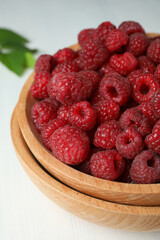Red juicy raspberries in a wooden bowl on a white wooden background