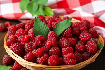 Raspberries in a wicker bowl and a tea towel on a wooden table