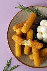 Plate with cheese sticks, mozzarella and rosemary on violet background