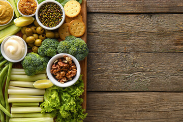 Board with different green vegetables and bowls with sauce on wooden background, closeup