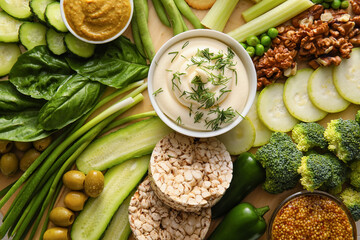 Different green vegetables, rice crackers and bowl with sauce as background
