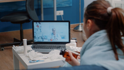 Obraz na płótnie Canvas Patient with flu using video call communication for healthcare consultation with doctor. Ill woman holding bottle of pills and tablet with capsules for treatment advice and medication.