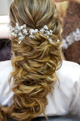 Blond Hair. Beautiful Caucasian Woman with Curly Long Hair. Bridal hairstyle decorated by white flowers