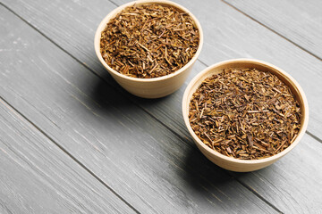 Bowls of dry hojicha green tea on grey wooden background