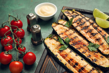 Wooden board with tasty grilled zucchini and fresh tomatoes on color background, closeup