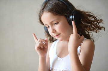 beautiful little curly girl in headphones listen music conducting with hands and fingers during...