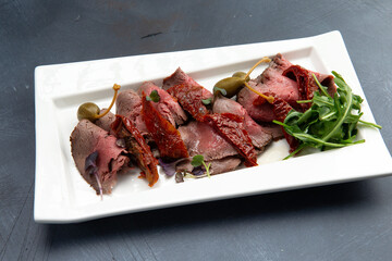 Snack. Meat, sun-dried tomatoes, capers and arugula in a plate.
