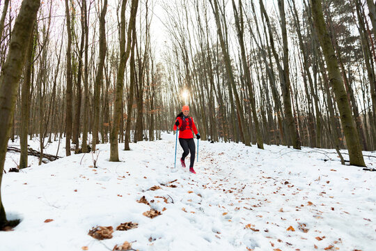 Woman Trail Running in Winter. Female Runner Jogging Downhill with Trekking Poles on Cold Winter Day.