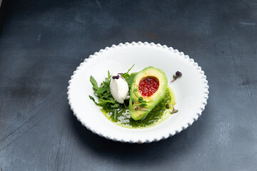 Snack. Avocado with red caviar and arugula in a plate.