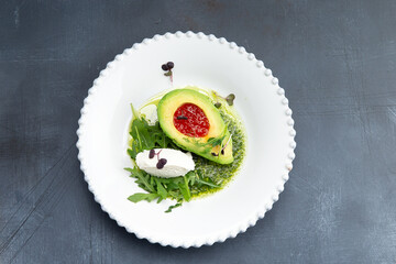 Snack. Avocado with red caviar and arugula in a plate.