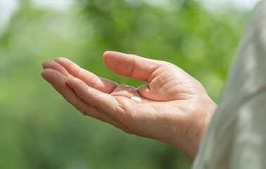 Hand of the elderly or middle-aged woman taking medicine in nature. 自然の中で薬を持つ高齢なまたは中高年の女性の手