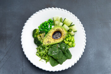 Snack. Avocado with beans, broccoli, zucchini and arugula on a plate.