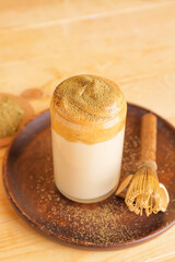 Glass of tasty dalgona hojicha latte and chasen on wooden background